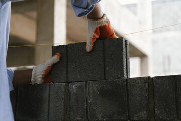 A skilled bricklayer works with mortar and trowel, carefully building a brick wall at a...