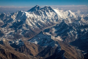 Aerial view of towering snow-capped mountain peaks and jagged ridges, a sun-drenched vista of rocky landscapes meeting a hazy, blue horizon