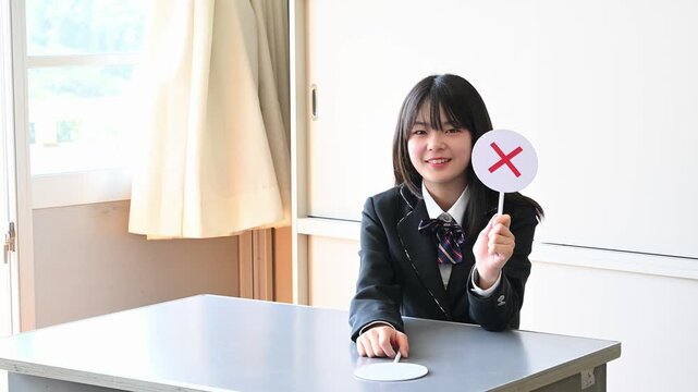 クイズに答える女子学生　学校の教室で○✕を出す教育イメージ