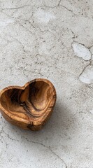 Heart-shaped wooden bowl sits on a textured gray surface. Warm light