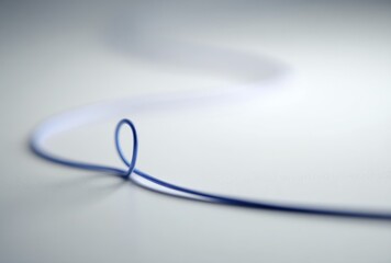 Wavy, blue thread lays on a bright white surface with gentle shadowing; a simple, minimalistic composition