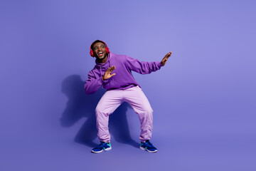 Cheerful young man in vibrant sportswear listening to music and dancing joyfully against a bold...