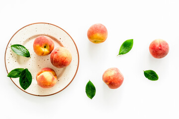 Red peaches pattern with plate and leaves on white table top-down