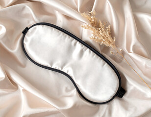 White sleep mask with black trim on silk sheet