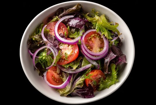 Overhead view of a fresh salad in a white bowl with vibrant red onions and sliced tomatoes, atop mixed leafy greens against a black background