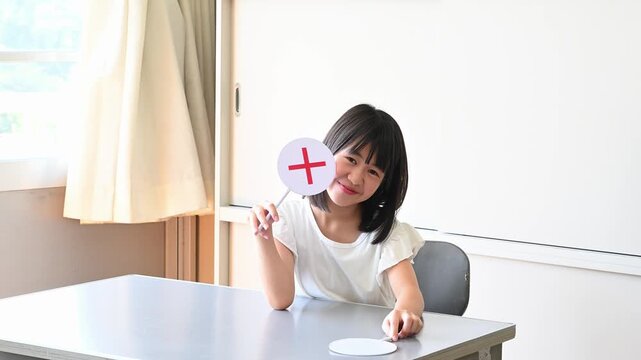 クイズに答える女子学生　学校の教室で○✕を出す教育イメージ