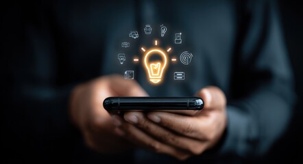 Person holding smartphone, glowing bulb above, with tiny icons. Dark, blurred background adds focus