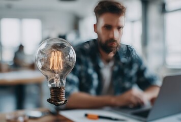 Blurred man with a beard works on a laptop, lightbulb floats next to him in office space