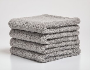 Stack of four fluffy, gray towels, neatly arranged on a clean, bright white surface with soft shadows