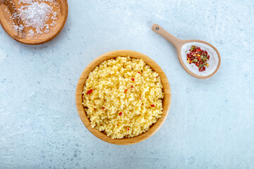 Cooked millet in a wooden bowl on a blue background, with salt and pepper, overhead flat lay shot. Healthy vegan side dish