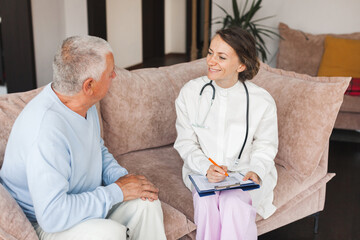 Obraz premium Female professional doctor showing medical test result explaining prescription using clipboard visiting senior elderly old man patient at home sitting on sofa