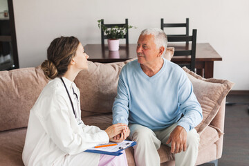 Obraz premium Female professional doctor showing medical test result explaining prescription using clipboard visiting senior elderly old man patient at home sitting on sofa