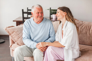 Obraz premium Happy adult daughter and senior father having fun enjoying talk sit on sofa at home