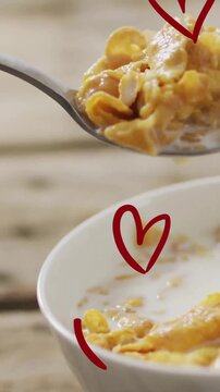 Spoon lifting cornflakes with milk, heart shapes animation over breakfast scene
