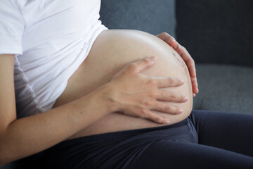 Expecting mother gently caressing her baby bump on a sofa