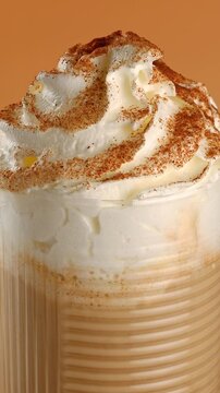 Glass of pumpkin latte with cream and spices close-up on a rotating table.