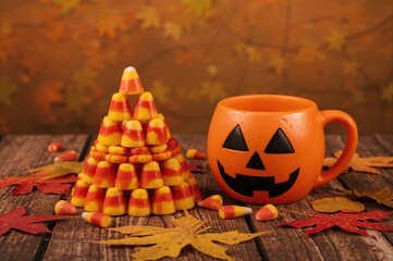 Autumn holiday theme featuring candy corn and a carved pumpkin mug on a rustic wooden surface
