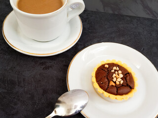 Pie brownies or pie with brownie filling and almond topping served with Kopi Susu or instant milk coffee. Selective focus in grey background.
