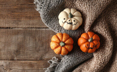Fototapeta premium Three small Halloween pumpkins on a scarf with a wooden background, top view 
