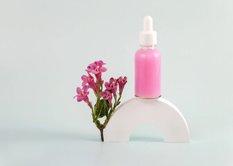 bottle of essential oil with a pipette and pink flowers on a white round podium. The concept of skin care using natural cosmetics