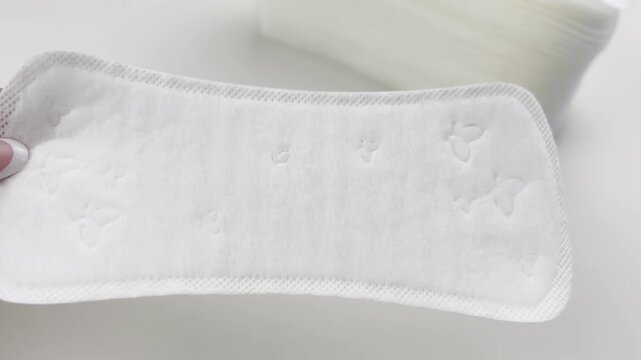 Woman hand holding and showing sanitary pad on white background, top view. Feminine hygiene, menstruation cycle, daily pads for menstrual care, intimate health, gynecology, women&rsquo;s healthcare