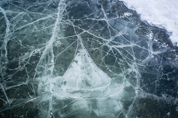 Obraz premium Detailed view of frozen water with complex fissures beneath the clear surface, bordered by snow-covered edges in a striking winter scene.