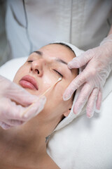 Beautician applying cosmetic treatment on female face with cotton swab in beauty salon