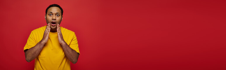 Stylish Indian man shows excitement in vibrant outfit against bold red backdrop