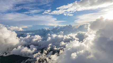 Stunning aerial perspective of fluffy white clouds beneath a blue sky with sunlight breaking through. A peaceful and inspiring natural landscape ideal for travel, aviation, weather, spirituality, and