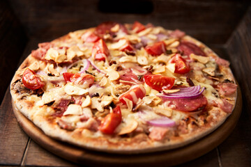 Pizza with salami, tomatoes and mozzarella cheese. Rustic wooden background. Soft focus. Copy space.	