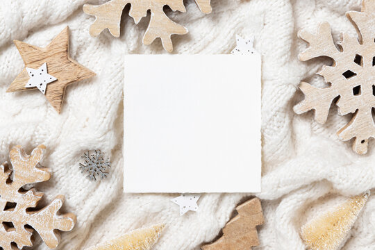 Square Blank card on white knitted sweater near wooden Christmas decor, Holiday mockup
