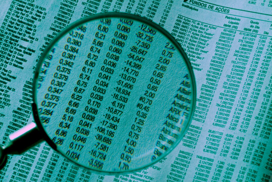 Jornal de not&iacute;cias de economia com uma lupa para analise dos dados das a&ccedil;&otilde;es