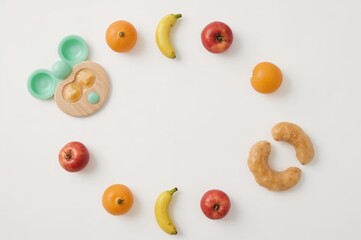Top view arrangement featuring infant feeding tools and plastic fruits on a pale surface. Initial baby nutrition theme