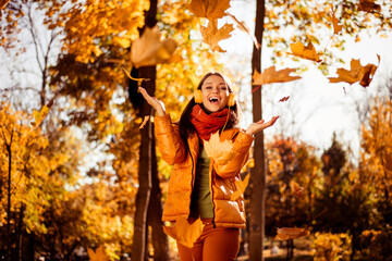 Young woman enjoying a sunny autumn day in a park surrounded by colorful leaves, wearing stylish seasonal clothing