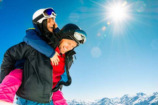 Happy young caucasian skiers couple in love having fun together playing in mountains piggybacking at wintertime. Couple ski isolated mock up outdoors blue winter banner copy space background