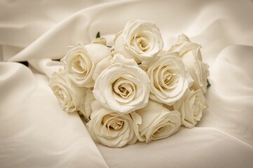 Obraz premium Elegant white roses on smooth white silk ideal for wedding backdrops in sepia tone.