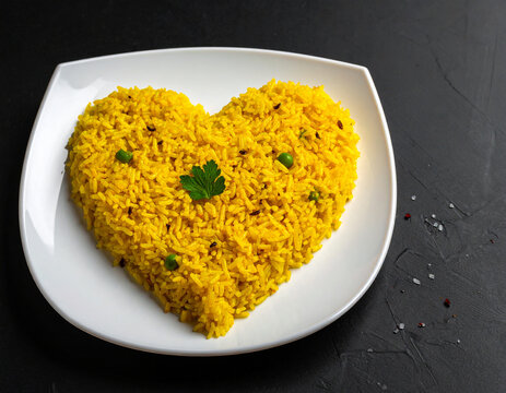 A plate of yellow rice shaped like a love heart. Isolated on a black background.