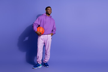 Young man in stylish purple hoodie with basketball posing against vibrant violet background representing leisure and energy