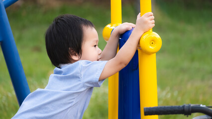 Fototapeta premium Portrait of a little boy having fun on exercise equipment in a playground. Asian child, 2-3 years old. Adorable kid having fun playing on the playground outdoors.