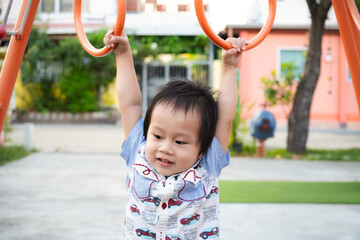 Little boy playing happily on the playground. Asian child training on monkey bars in summer park. Adorable son aged 2-3 years old.
