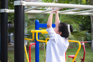 Fototapeta premium Blurry of a girl is hanging and reaching out to change grips on a monkey bar. This image shows the physical activity of an 8-9 year old child in an outdoor playground. Exercise for good health.