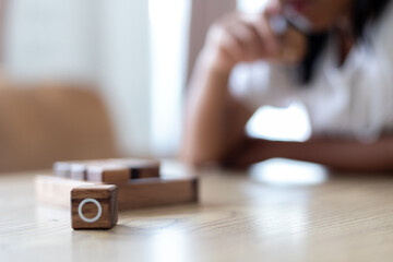 Fototapeta premium Close-up wooden O block from a tic-tac-toe game with a child thinking in the background, concept of childhood learning, focus, decision making, and strategy.