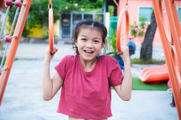 Asian cute young girl plays on the playground on a summer or spring day. Kid hanging on playground rings in park. Adorable child aged 9-10 years old.