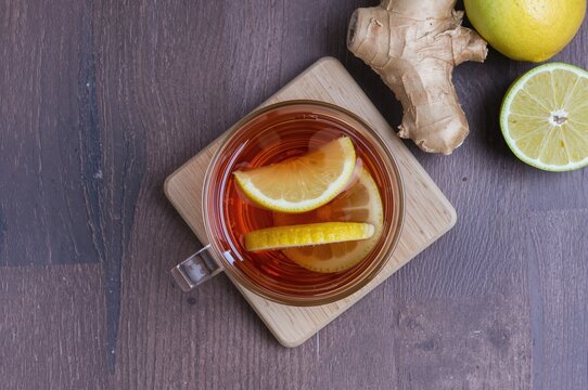 Glass cup of steaming ginger tea with lemon and honey on rustic wooden boards. Natural remedy for cold and flu, overhead view