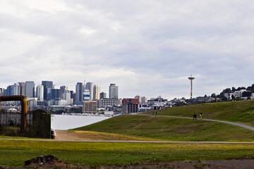 Scenic view of Seattle skyline with Space Needle, waterfront, grassy park, and industrial pipes...