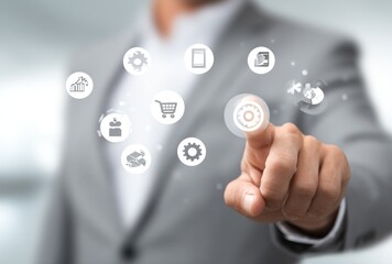 Man in a suit touches a floating digital display with icons. Finger on the gear, other icons surrounding