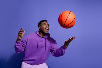 Energetic young man in purple hoodie playing basketball, excited and stylish, posing against...