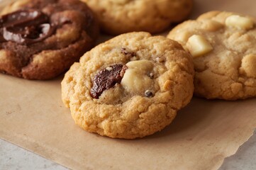 Close-up view of various cookies including chocolate chip, oatmeal raisin, and white chocolate on parchment paper with space for text