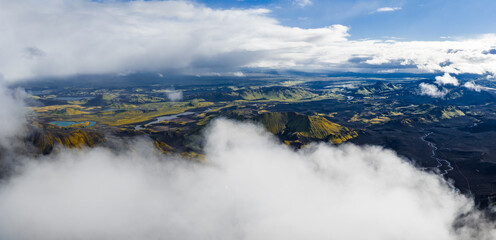 Fototapeta premium Aerial perspective of Iceland's landscape with volcanic craters, winding rivers, scattered lakes, vibrant terrain, and low hanging clouds.