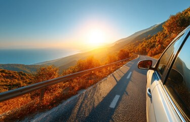 Bright sunset view from a car driving on an winding scenic mountain road by the sea. Warm, autumnal colors, clear blue sky, metal barrier